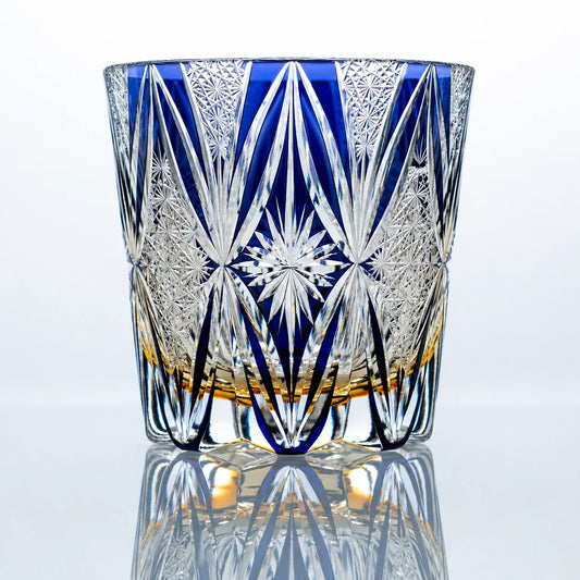 A hand-cut Edo Kiriko crystal whiskey glass featuring a vivid blue upper body, clear geometric cut details, a central starburst motif, and a polished reflective studio presentation.