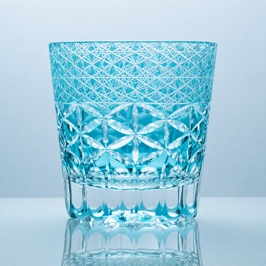 A hand-cut Edo Kiriko whiskey glass in luminous aqua crystal, featuring dense star-lattice engraving, interlocking petal-style geometric cuts, and a clear sculpted crystal base.