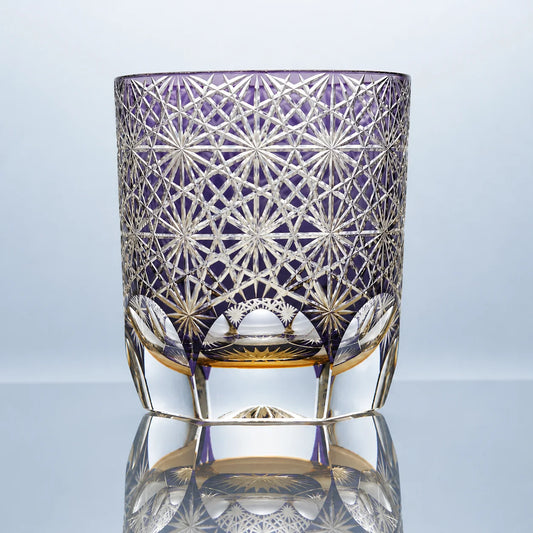 A small hand-cut Edo Kiriko crystal whiskey glass featuring a soft violet tone, intricate daisy-inspired starburst patterns, and a polished faceted base in a clean studio setting.