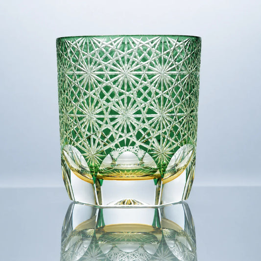 A small green hand-cut Edo Kiriko crystal whiskey glass featuring daisy-inspired starburst patterns, a soft emerald tone, and a polished clear faceted base in a reflective studio setting.