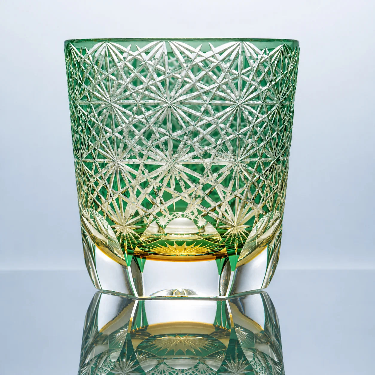A large green hand-cut Edo Kiriko crystal whiskey glass featuring dense daisy-inspired starburst cut patterns, a vivid green tone, and a polished clear base in a reflective studio setting.