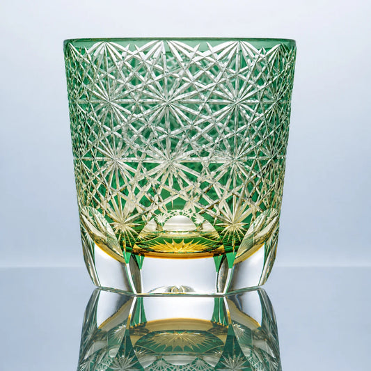 A large green hand-cut Edo Kiriko crystal whiskey glass featuring dense daisy-inspired starburst cut patterns, a vivid green tone, and a polished clear base in a reflective studio setting.