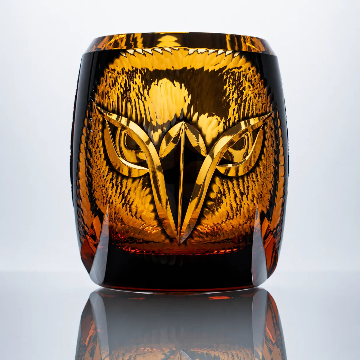 An amber hand-cut Edo Kiriko whiskey glass featuring a sculptural owl motif, rich golden crystal tones, and a reflective studio presentation.