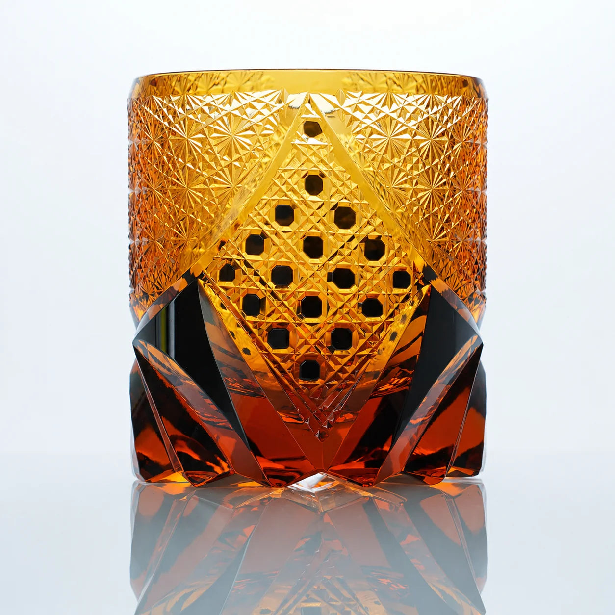 A front view of the Black Warrior hand-cut Edo Kiriko whiskey glass featuring amber crystal tones, a geometric hexagonal center panel, and bold dark faceted details.