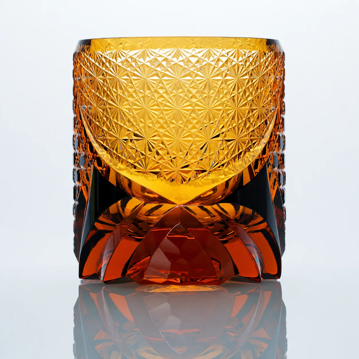 A back view of the Black Warrior hand-cut Edo Kiriko whiskey glass featuring dense starburst cut patterns, warm amber crystal tones, and a sculpted faceted base.