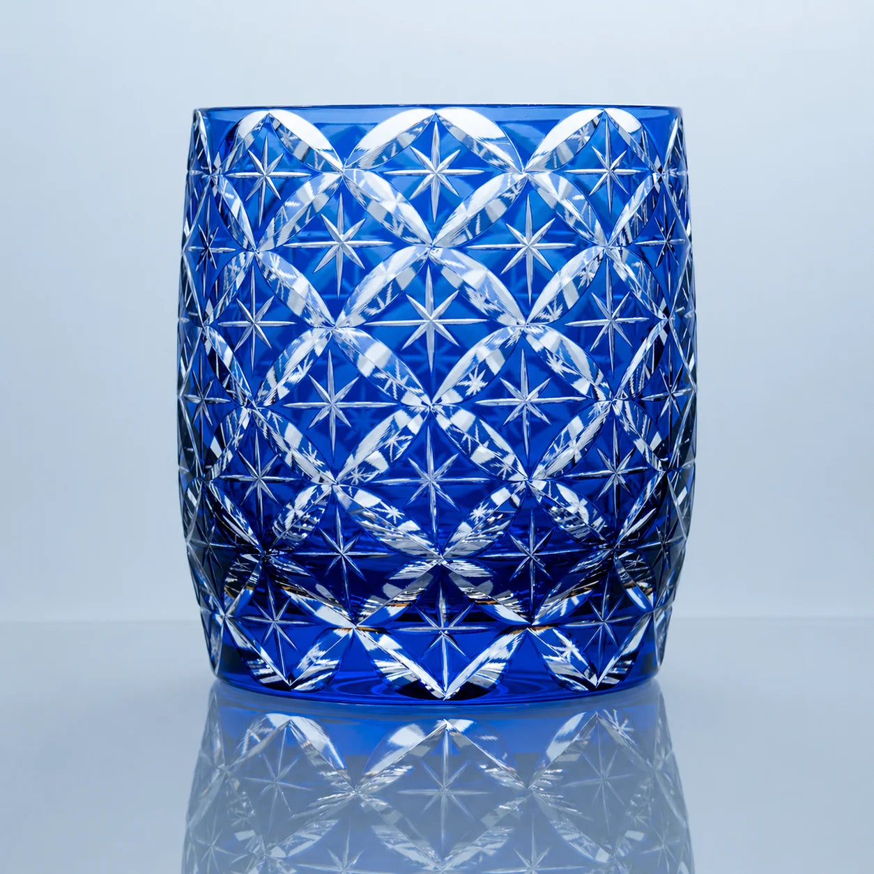 A blue hand-cut Edo Kiriko whiskey glass featuring repeating star motifs, an intricate geometric lattice pattern, and a polished reflective studio presentation.