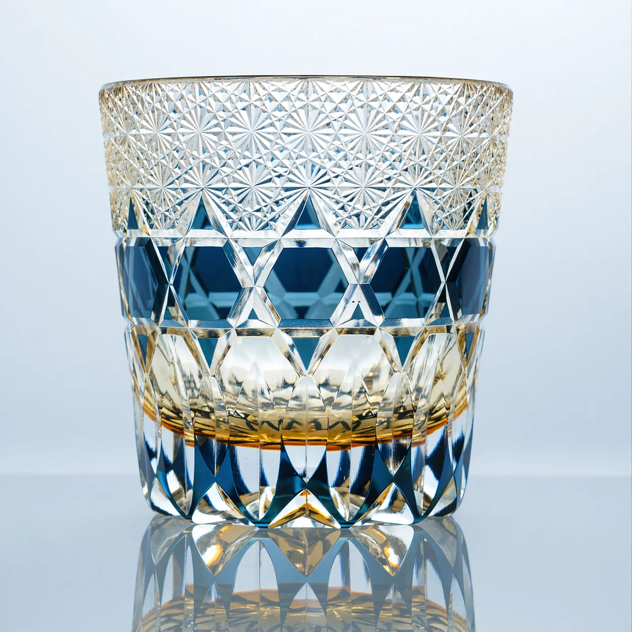 A blue hand-cut Edo Kiriko whiskey glass featuring dense crystal starburst cuts, a vivid blue geometric band, and a polished reflective studio presentation.