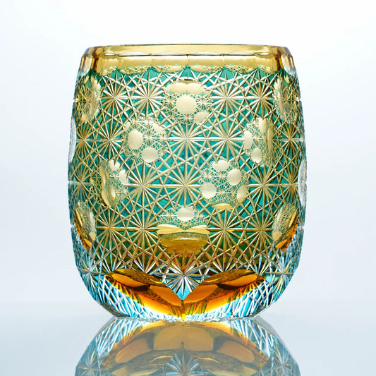 An aqua amber hand-cut Edo Kiriko whiskey glass featuring teal-green crystal tones, warm amber accents, intricate starburst patterns, and a reflective studio presentation.