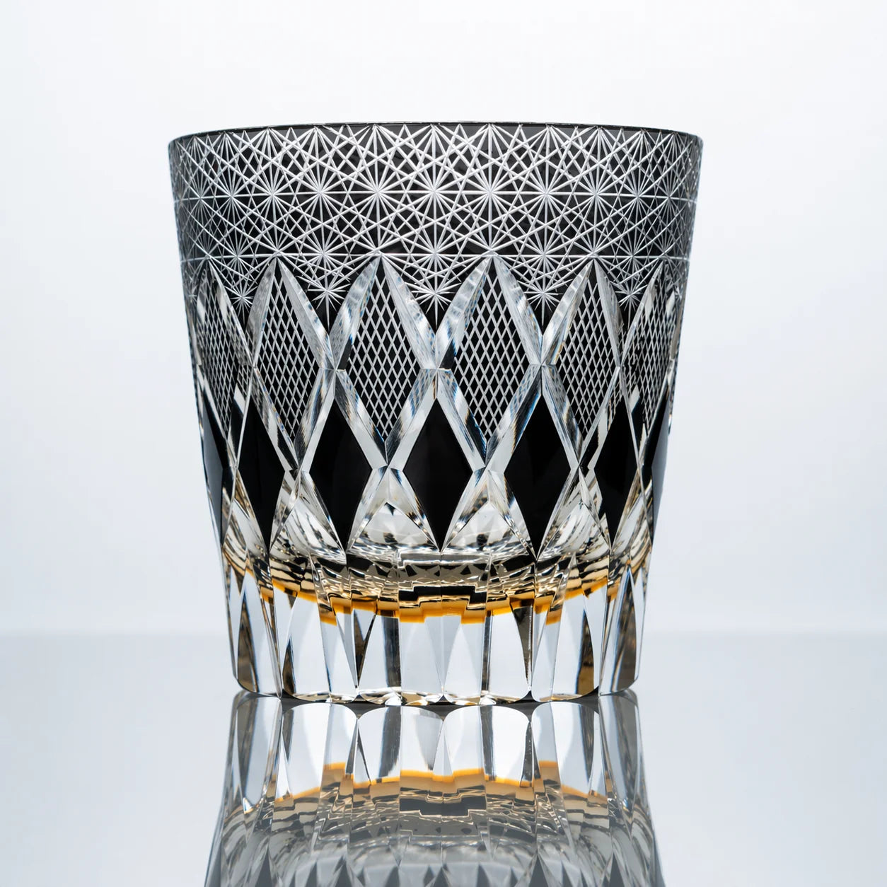 A smoke black hand-cut Edo Kiriko whiskey glass featuring sharp diamond lattice cuts, dense starburst crystal patterns, and a polished reflective studio presentation.