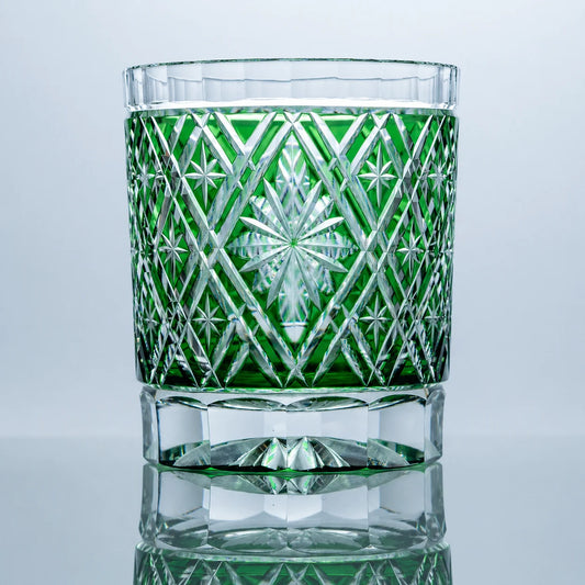 An emerald hand-cut Edo Kiriko whiskey glass featuring a radiant starburst center, geometric lattice crystal cuts, a clear faceted base, and a polished reflective studio presentation.