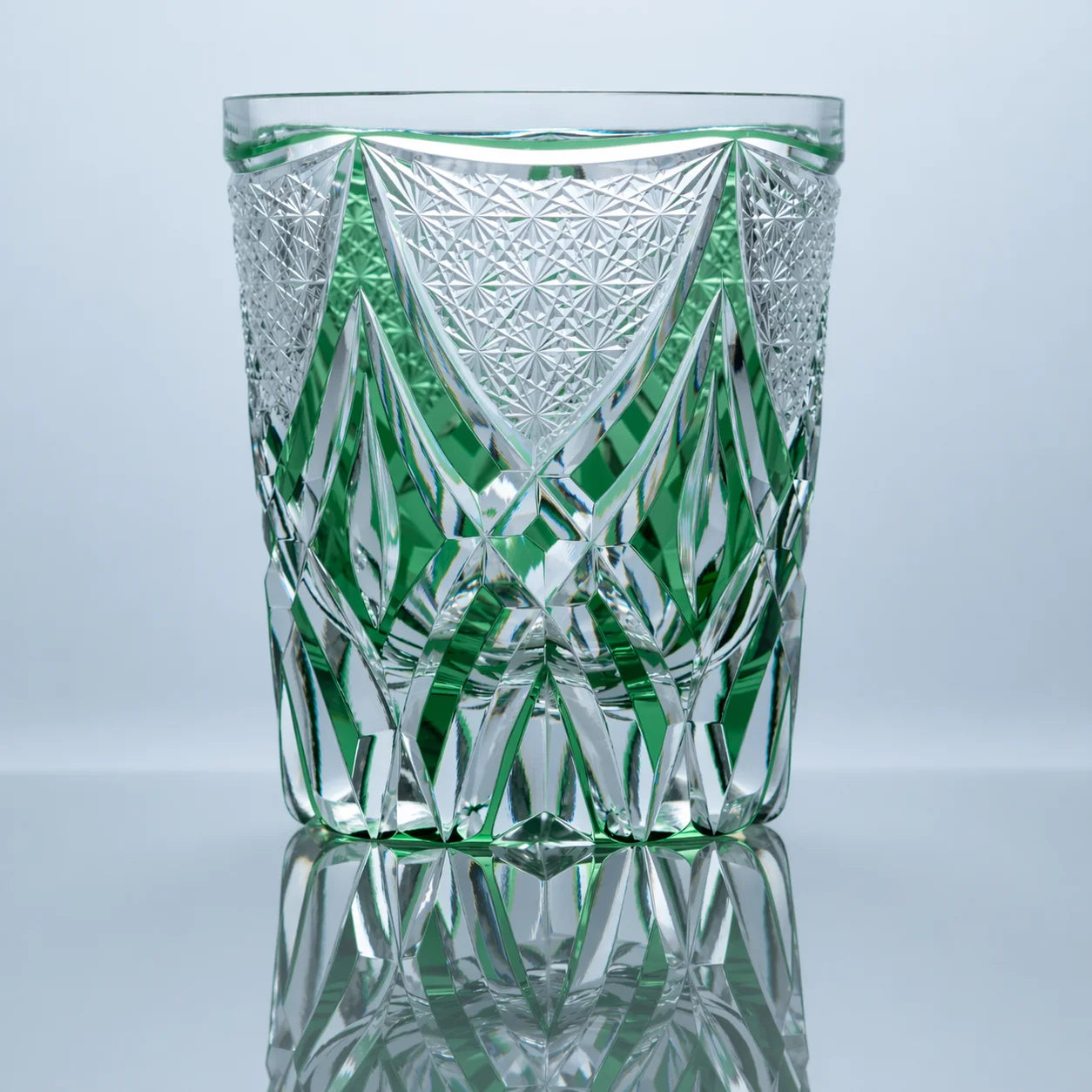 A hand-cut emerald Edo Kiriko whiskey glass featuring a central shield-like crystal motif, sharp geometric facets, and a polished reflective studio presentation.