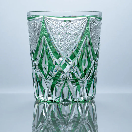 A hand-cut emerald Edo Kiriko whiskey glass featuring a central shield-like crystal motif, sharp geometric facets, and a polished reflective studio presentation.