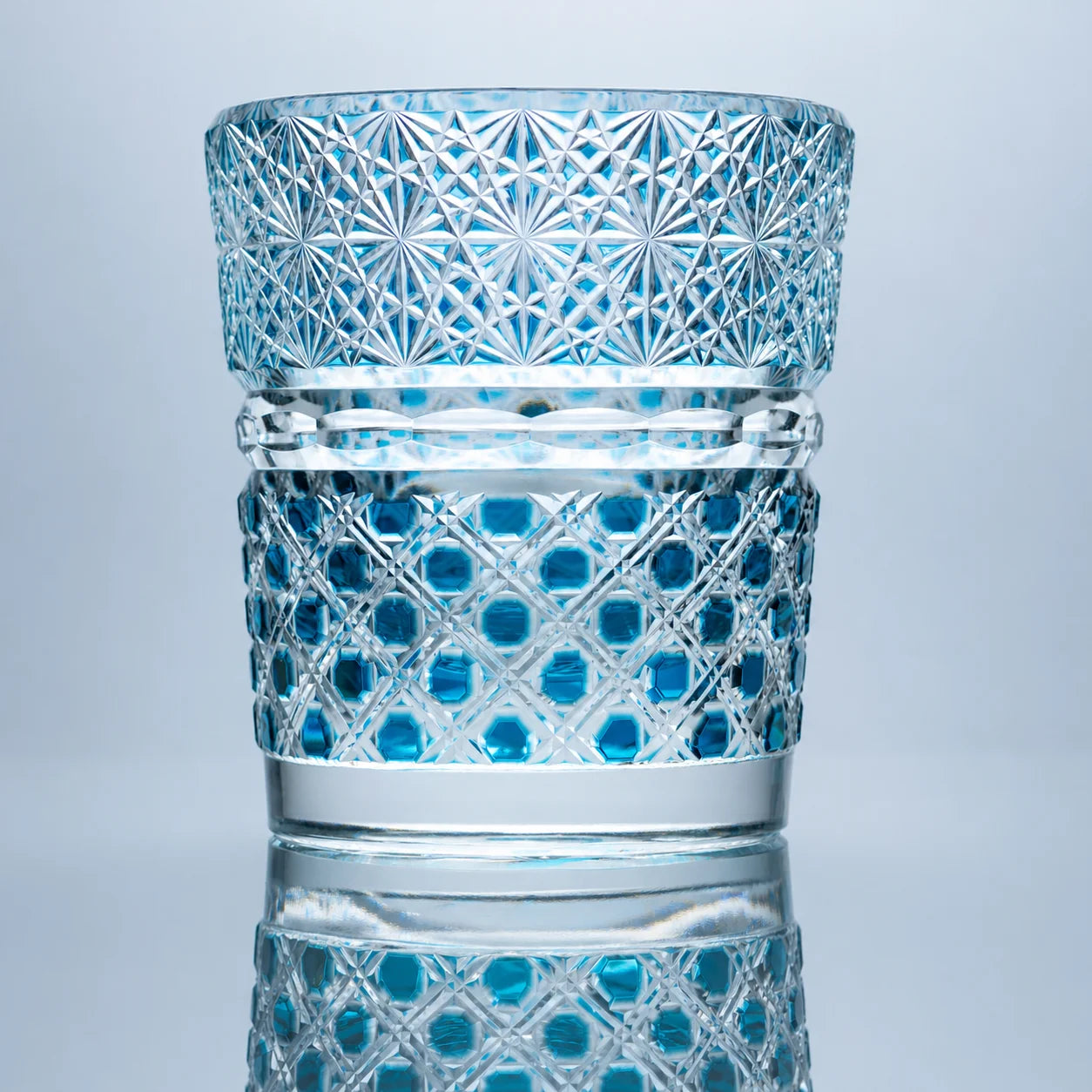 A hand-cut aqua Edo Kiriko whiskey glass featuring jewel-like circular crystal cuts, intricate starburst patterns, clear polished bands, and a reflective studio presentation.