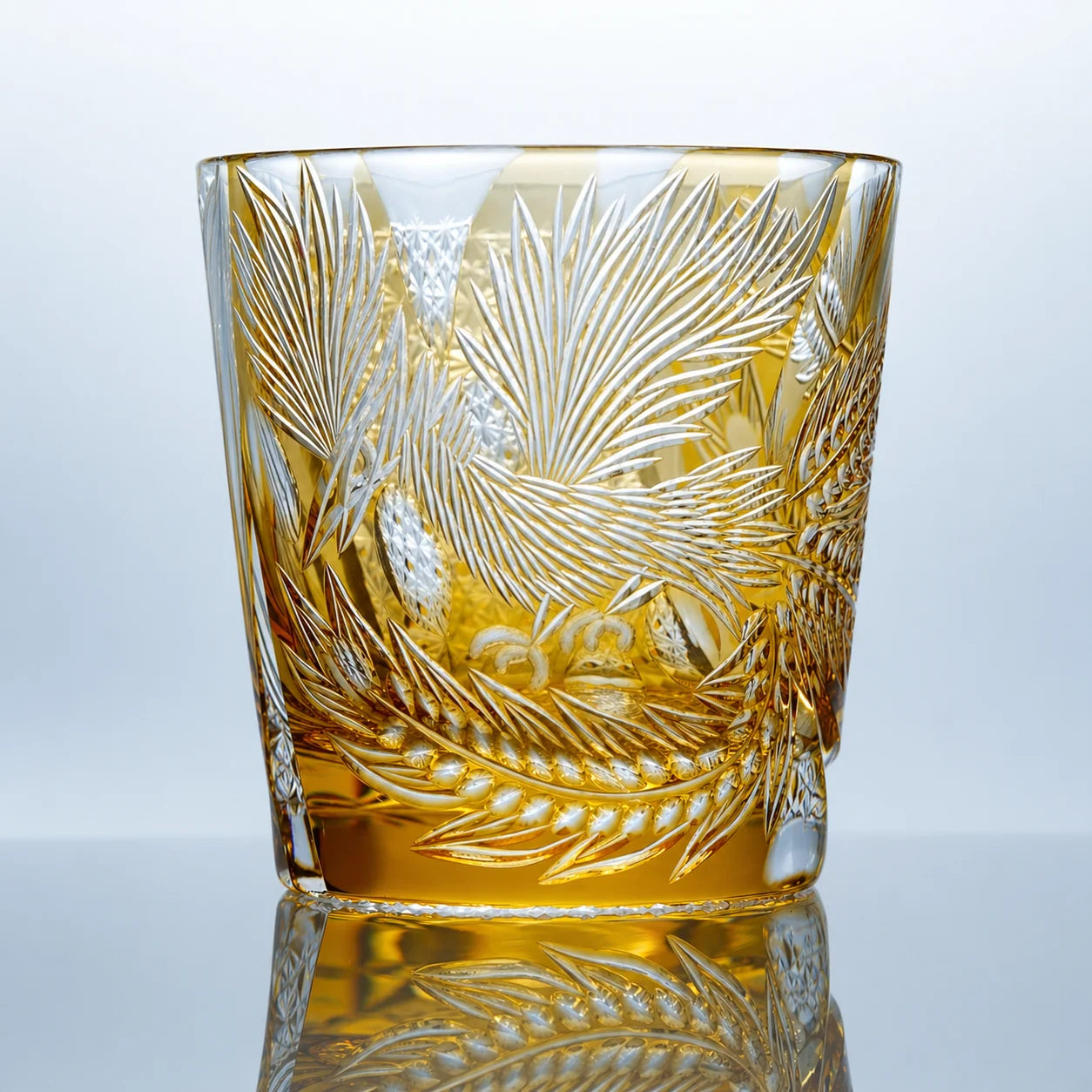 A hand-cut amber Edo Kiriko whiskey glass featuring phoenix-inspired feather motifs, intricate geometric patterns, polished crystal surfaces, and a reflective studio presentation.