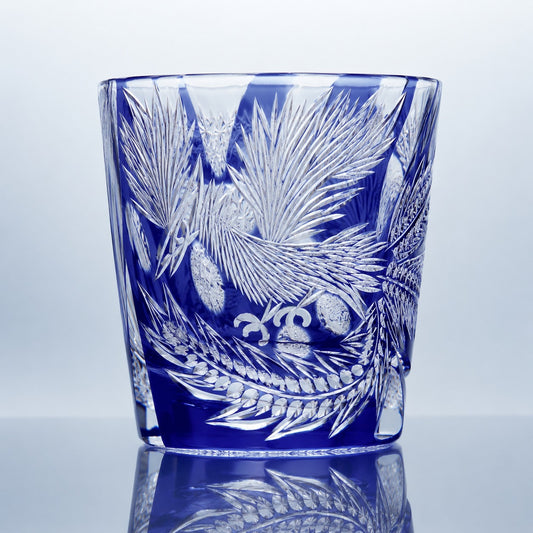 A sapphire blue hand-cut Edo Kiriko whiskey glass featuring phoenix-inspired feather motifs, flowing engraved details, and a reflective studio presentation.