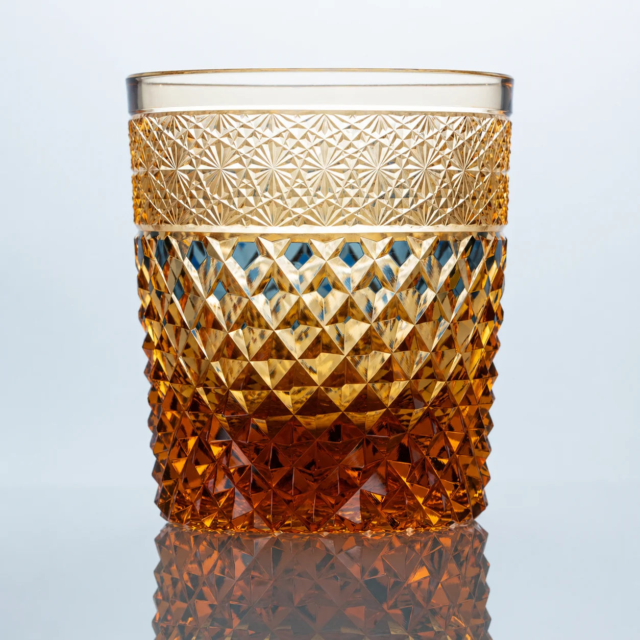 A hand-cut amber Edo Kiriko whiskey glass featuring warm golden tones, diamond-like crystal facets, intricate starburst detailing, and a polished reflective studio presentation.