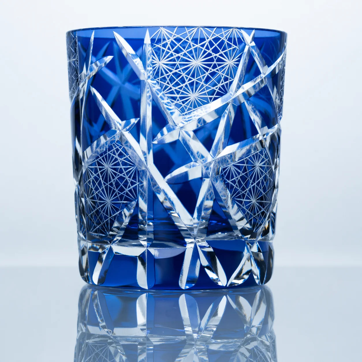 A sapphire blue hand-cut Edo Kiriko whiskey glass featuring bamboo-inspired crystal cuts, geometric starburst textures, clear faceted detailing, and a reflective studio presentation.