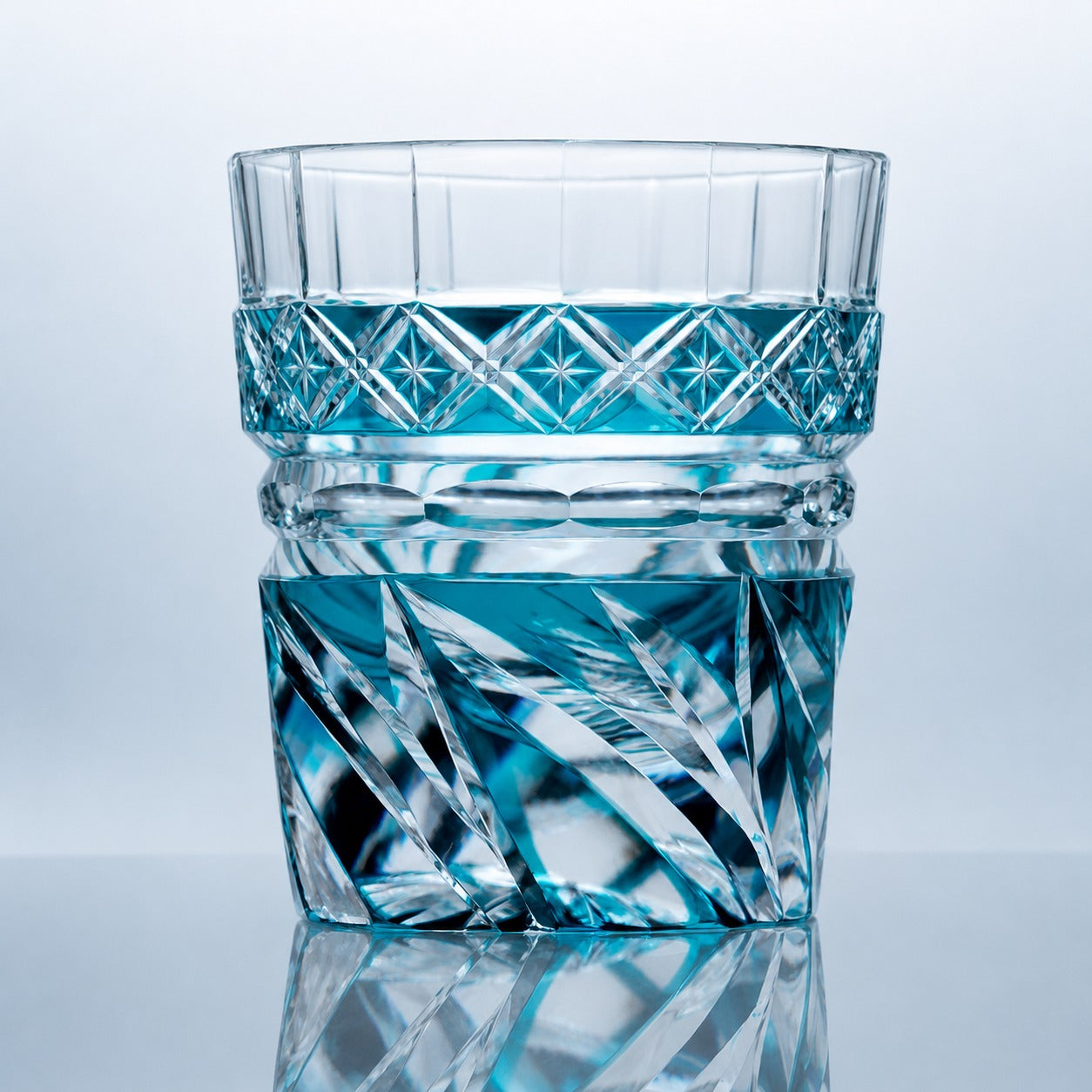 A hand-cut aqua Edo Kiriko whiskey glass featuring bright blue crystal tones, wave-like prism cuts, star-detailed banding, and a reflective studio presentation.