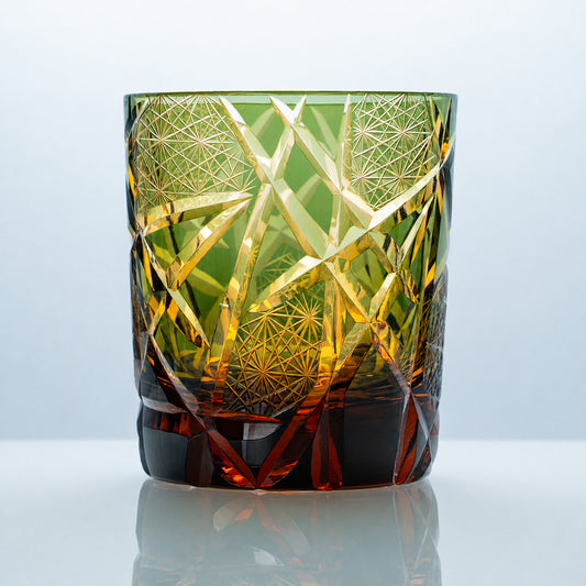 A hand-cut Edo Kiriko whiskey glass featuring olive green crystal tones, glowing amber accents, fine star-lattice panels, and bold angular crystal facets.