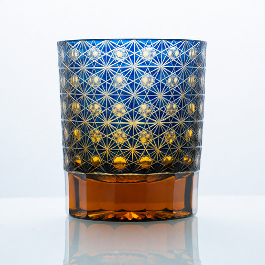 A hand-cut Edo Kiriko whiskey glass featuring a cobalt-blue crystal body, intricate Asanoha-style lattice engraving, and a warm amber-toned base.